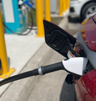 Electric vehicle charging port plugged into red electric vehicle and charging.